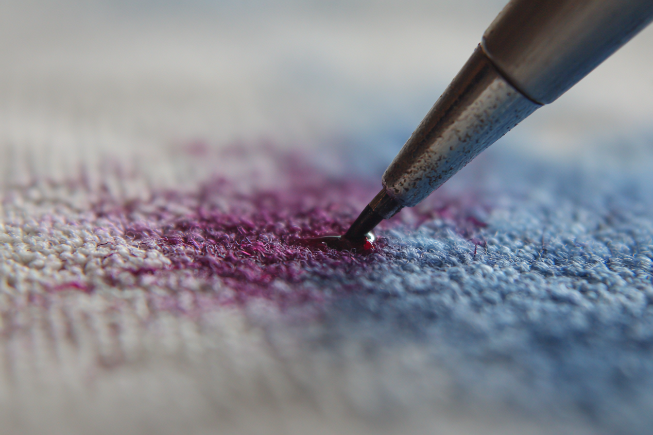 Ponta de caneta tocando mancha roxa em carpete
